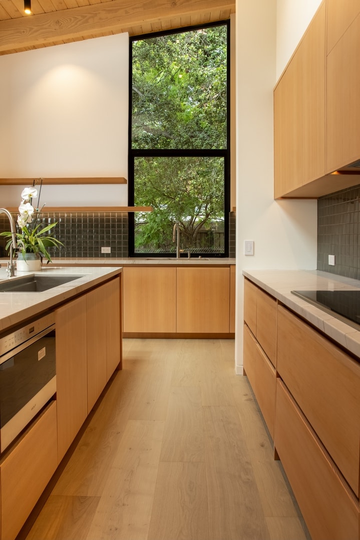 Kitchen with floor-to-ceiling black-frame window framing a lush tree canopy — La Cañada